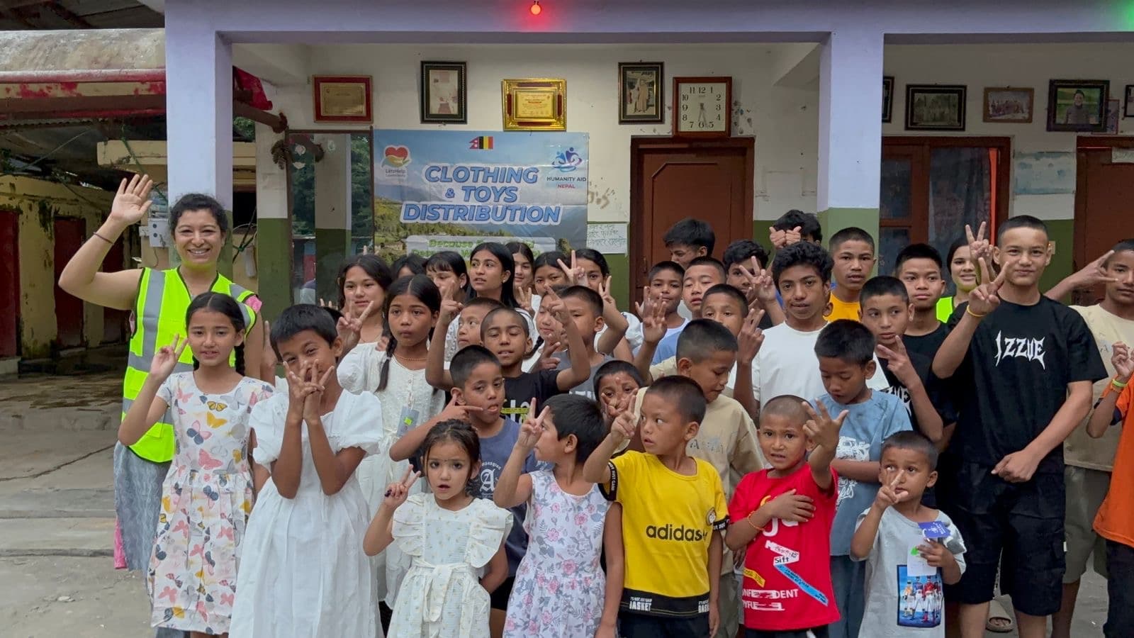 Children and a volunteer waving in front of a Clothing & Toys Distribution banner at a children's home