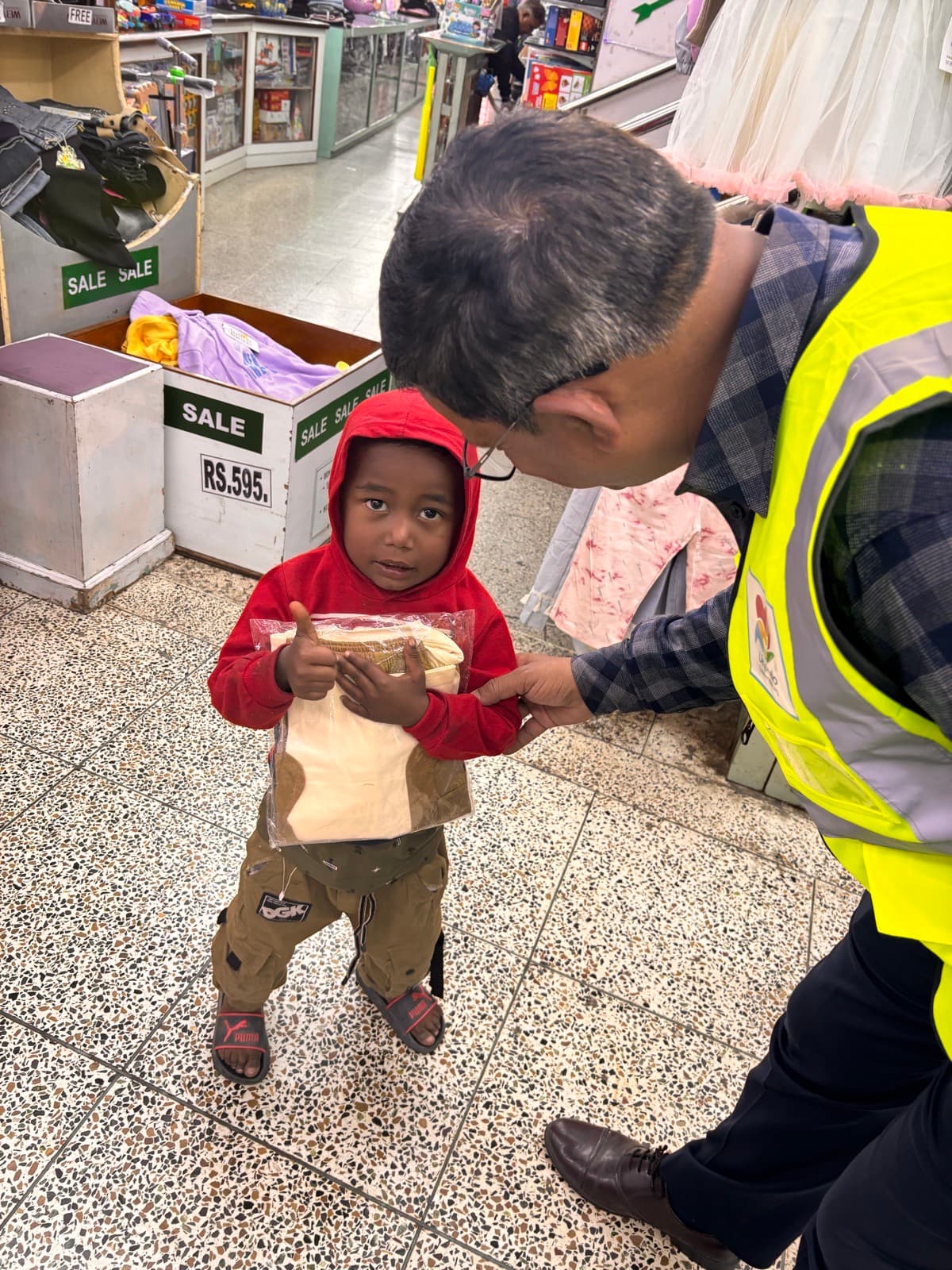 A small child in a new jacket next to a volunteer in a shop