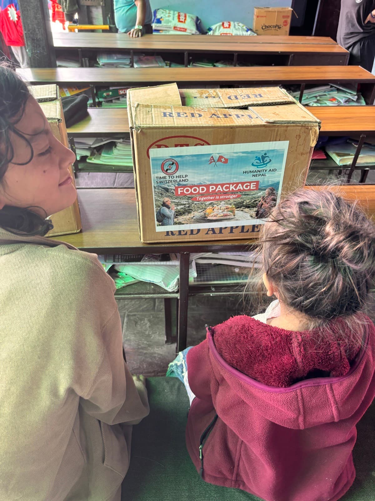 Two girls sitting next to a food package box