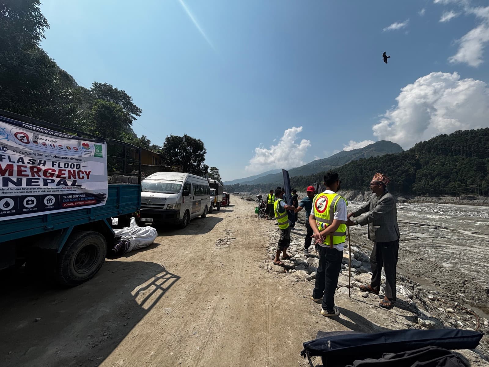 TimeToShare volunteers in high-visibility vests next to a relief truck on a road through the flood area