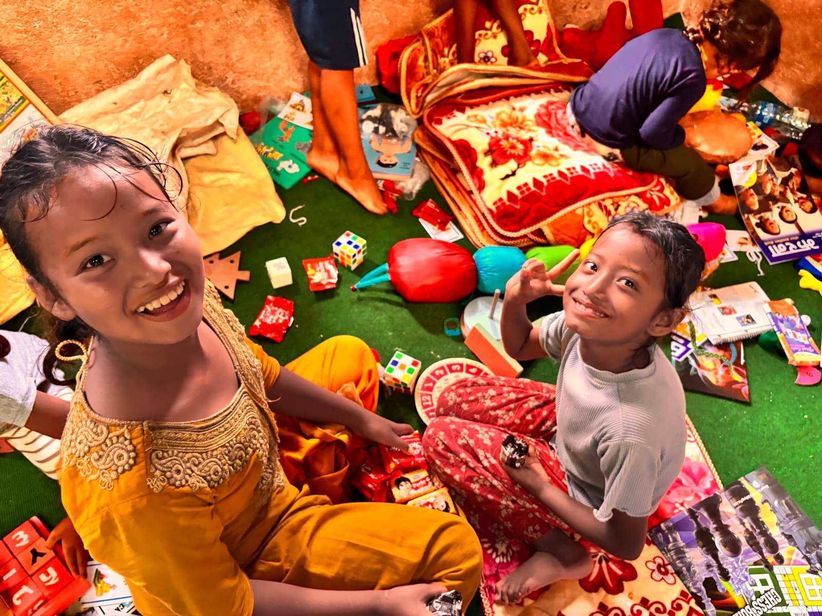 Two smiling girls sitting among household items received after the floods