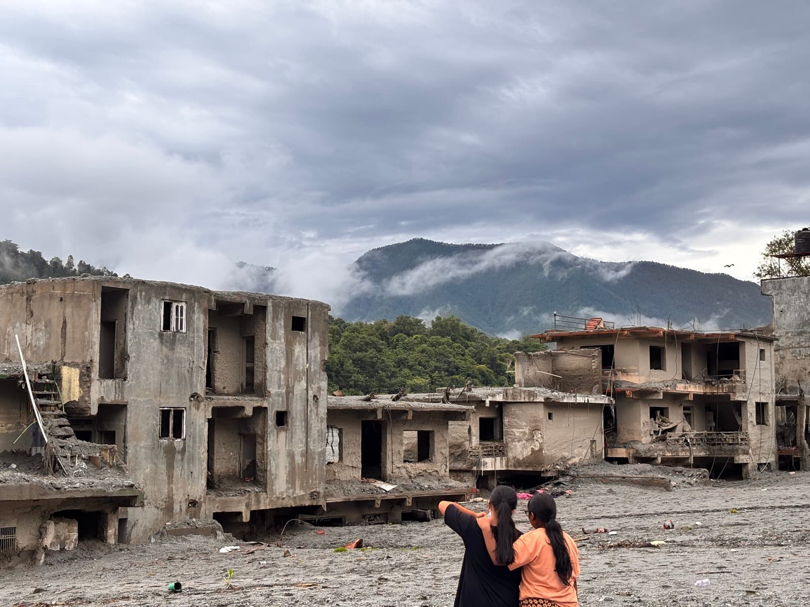 Two people looking at flood-damaged buildings in a valley