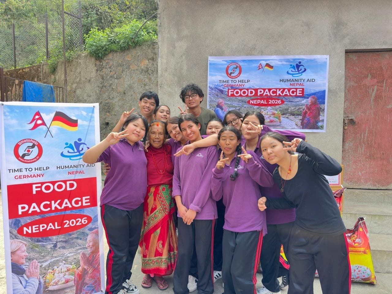 Student volunteers in purple uniforms posing with an older woman next to food package banners