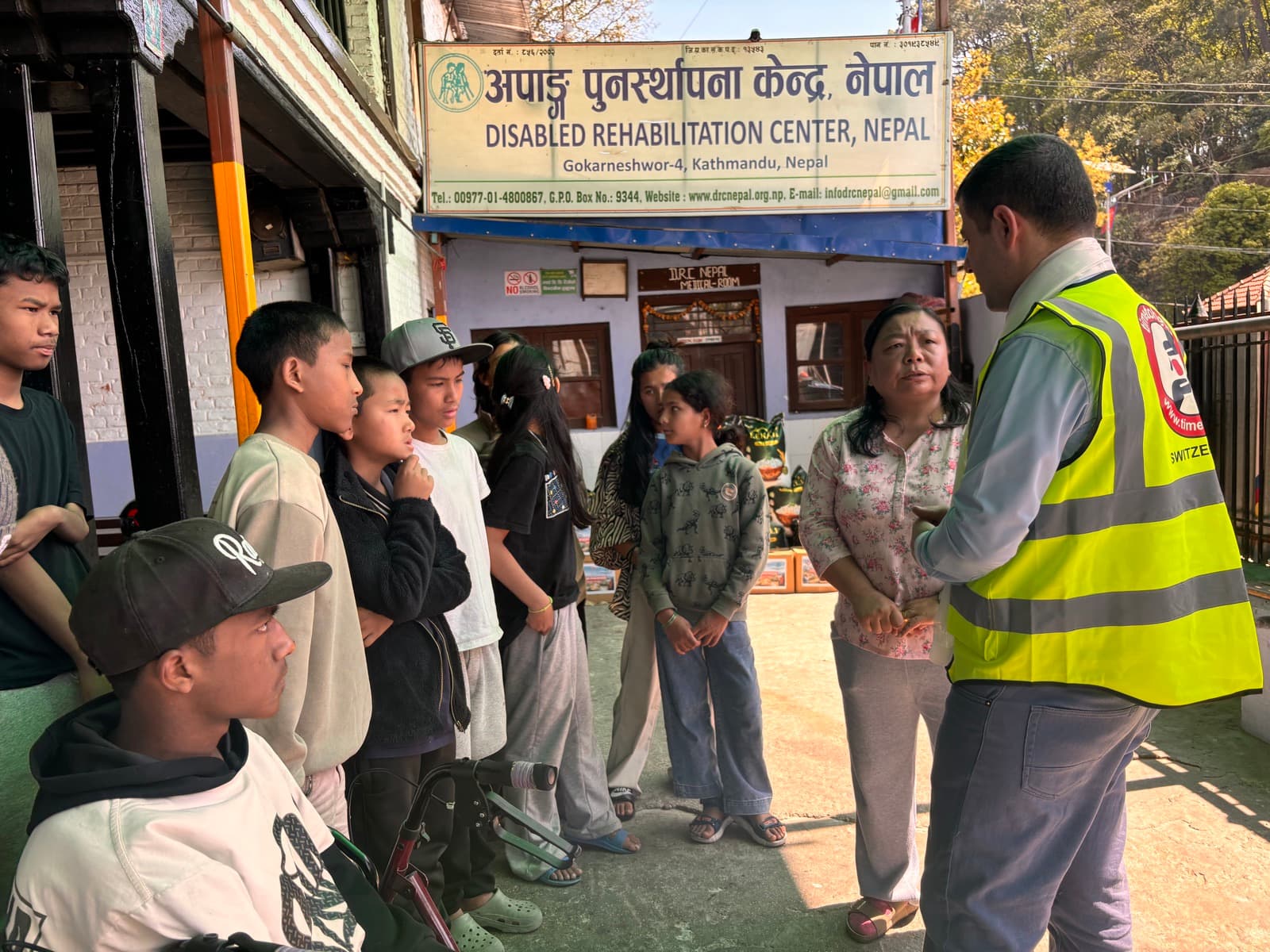 A volunteer talking with young people and staff in front of the Disabled Rehabilitation Center
