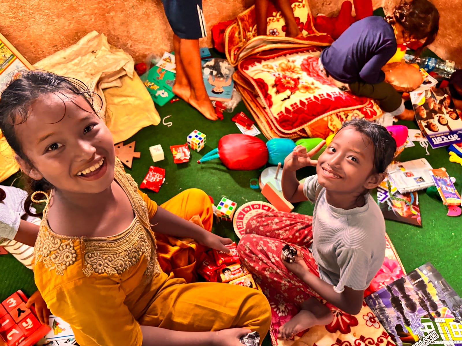 Two smiling girls sitting among household items received after the floods