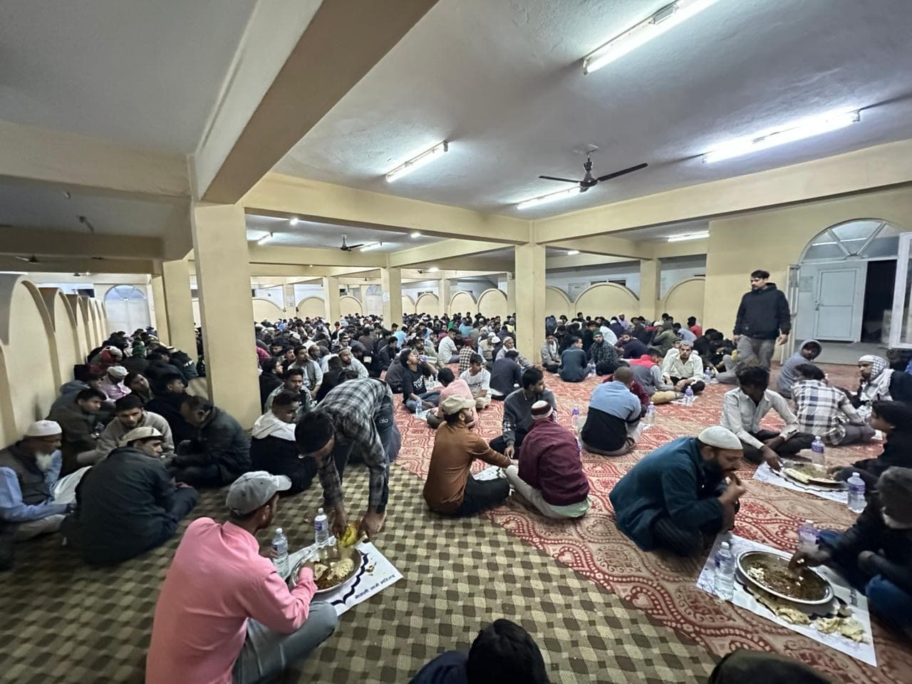 A large hall full of people sitting on the floor for a community iftar